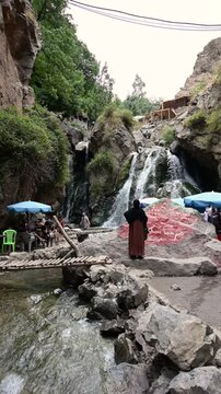 Marrakech, morocco. August 9, 2026. Beautiful waterfall cascading down rocks in the ourika valley, morocco. A woman in traditional dress observes the flowing water and scenery