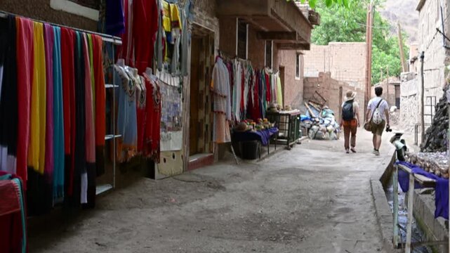 Marrakech, morocco. August 9, 2026. Couple of tourists walking down a narrow street in a traditional moroccan village, passing by shops selling colorful clothes and souvenirs