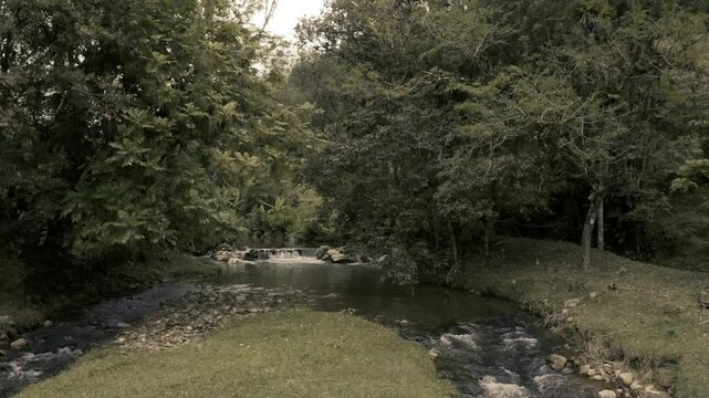 Paisagem rural com riacho de &aacute;guas calmas e caminho de terra em meio &agrave; natureza verdejante.