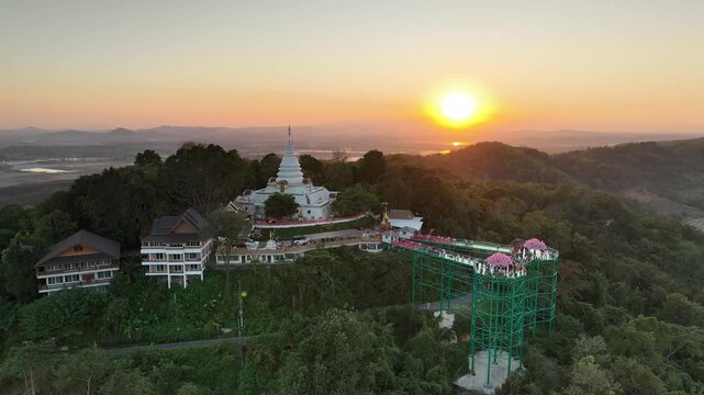 Aerial view of the temple and skywalk during sunset. The elevated complex is framed by forest, hills, and evening light in year 2023