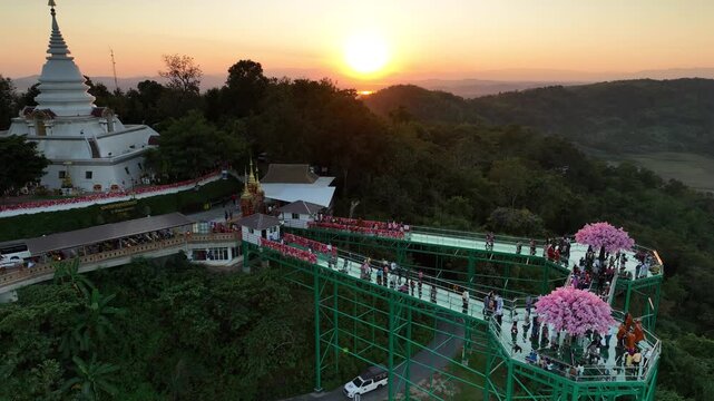 Skywalk at Wat Phrathat Pha Ngao silhouetted against the sunset. The elevated walkway forms a distinct outline above the forest in year 2023