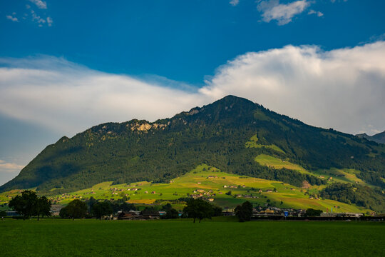 Mountain landscape in warm summer sunlight. Mountain scenery across a green valley. Summer light brightens mountain and pastures. Scenic countryside surrounds mountain in Switzerland.