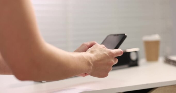 Woman with phone adjusting volume on portable audio speaker at white table indoors, closeup