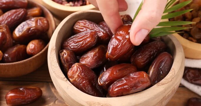 Woman putting bowl with tasty dried dates and taking one from wooden table, closeup