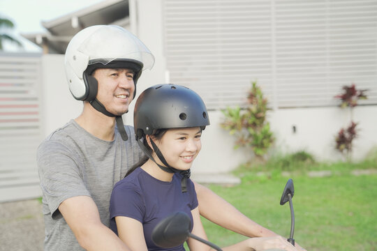 father daughter riding scooter motorcycle with helmet safety, family enjoy a sunny day ride together through a  suburban neighborhood 