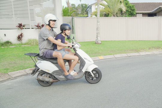 father daughter riding scooter motorcycle with helmet safety, family enjoy a sunny day ride together through a  suburban neighborhood 