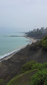 High angle aerial view of Costa Verde highway and Miraflores cliffs in Lima, Peru, featuring traffic along the Pacific Ocean coastline under an overcast sky. Ideal for editorial, travel, tourism, and 