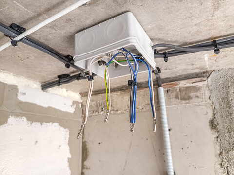 Electrical junction box with multiple colored wires attached to the ceiling. The setting is an unfinished room with exposed walls and ceiling.