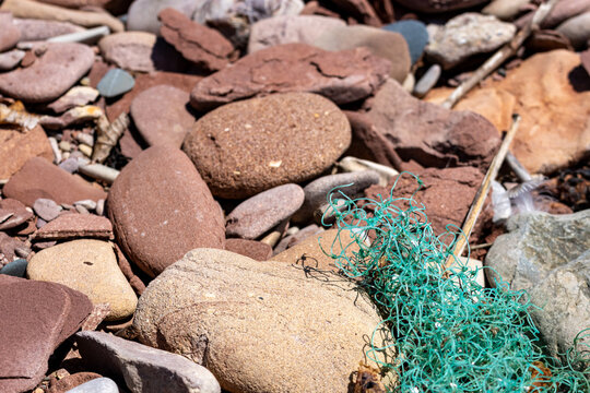 Gaspesie, Canada, 17 June 2026 : Green plastic netting debris lies tangled among various rocks and pebbles on a sunlit shore.