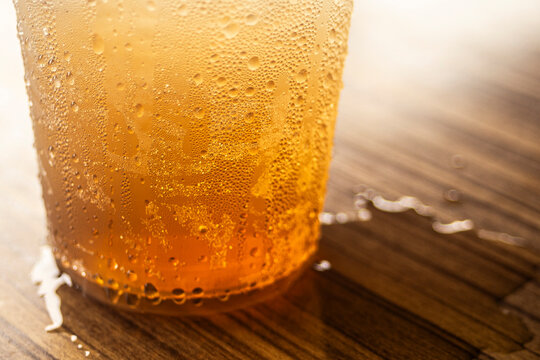 Close up of iced tea or amber beverage with condensation droplets on a wooden table.A refreshing close-up macro shot of a cold amber-colored beverage, such as iced tea, craft beer, or apple juice