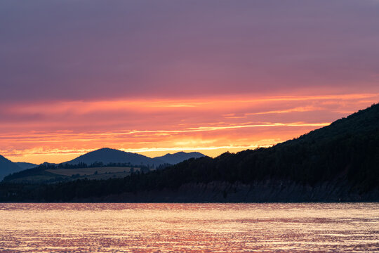 Gaspesie, Canada, 20 August 2026 : Vibrant sunset colors illuminate a tranquil lake and forested hills under a dramatic sky