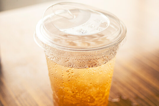 High angle close up of iced amber drink in a plastic cup with flat lid.A high-angle close-up shot of a cold amber-colored beverage, such as iced tea, apple juice, or kombucha