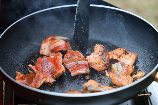 Seasoned pieces of wild Coho salmon sizzle in a hot pan near the Egegik River in Alaska, releasing steam and rich aroma during outdoor cooking after a successful catch.