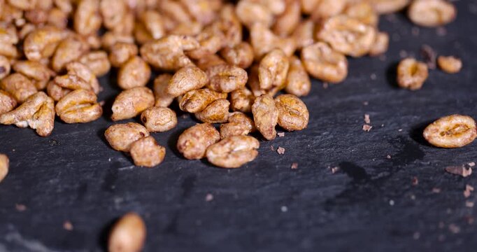 Brown chocolate puffed wheat grains on black slate stone, sweet breakfast cereal puffed wheat pieces scattered on kitchen table counter