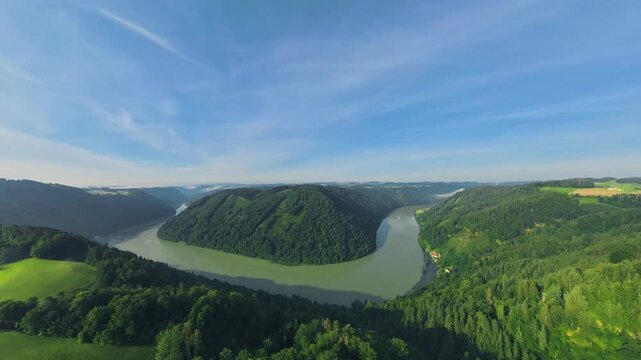 Drone footage flying backward from the Danube River into the M&uuml;hlviertel. The river recedes as green fields, forests and a rural village emerge beneath lingering low clouds.