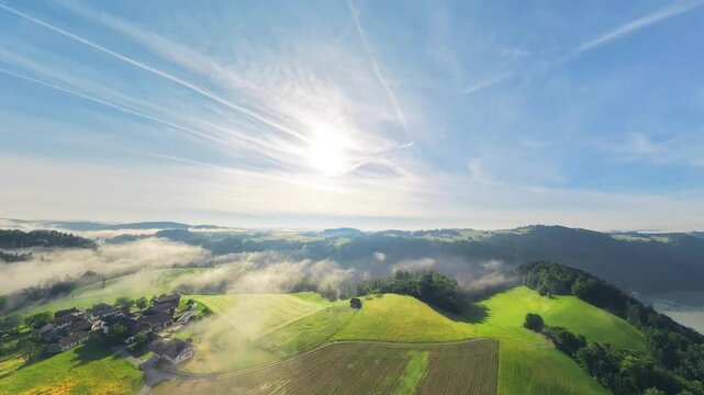 Drone footage over the sunny M&uuml;hlviertel in Upper Austria. Low clouds linger above green fields and a small farming village, with the Danube River visible in the distance.