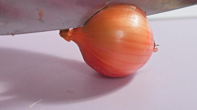 Close-up of kitchen cleaver blade cutting through an unpeeled yellow onion
