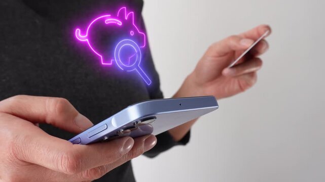 Financial planning. Businesswoman holding a bank card while holding a smartphone displaying a virtual piggy bank icon and a magnifying glass.