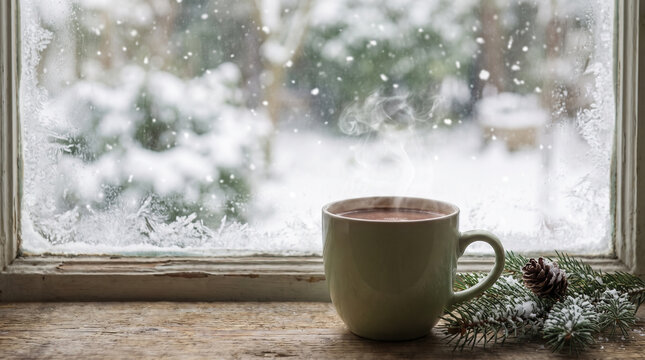 Steaming cocoa mug on a windowsill with snow falling outside