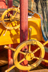 Wooden model of pirate sea ship with yellow steering wheels and red mast. Detail of children playground ship for kids games. Nautical adventure and imagination concept for childhood play. © Lassi M