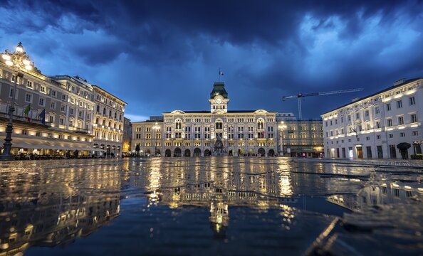 Illuminated square Piazza Unit&agrave; d'Italia, Town Hall, Palazzo Communale, with reflection, dramatic clouds, blue hour, old town, Trieste, Friuli-Venezia Giulia region, Italy