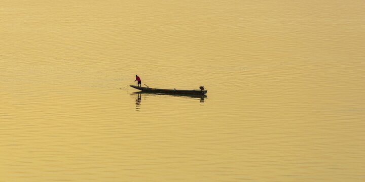 Fisherman with longtail boat (Thai: Ruea Hang Yao) at sunrise, Mekong between Thailand and Laos