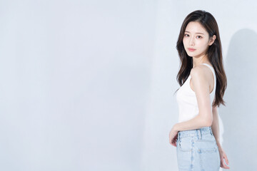 Obraz premium 白いタンクトップとデニム姿で立つ若い日本人女性、余白を生かした爽やかなライフスタイルポートレート