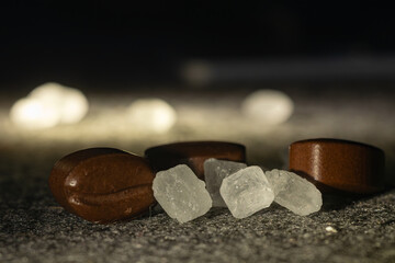 Naklejka premium Close-up of coffee bean shaped candies mixed with translucent rock sugar crystals on dark surface