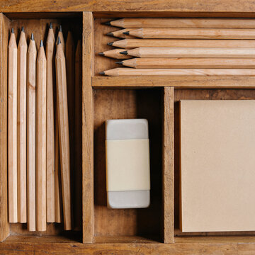 Wooden desk organizer with pencils, eraser and paper, warm art supplies still life