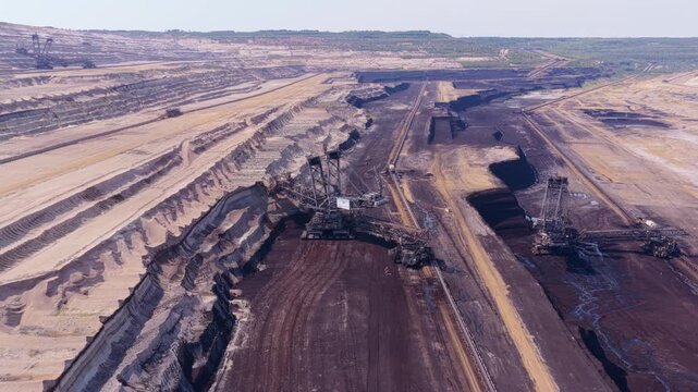 Massive bucket wheel excavator machines operating in a vast open pit coal mine. Aerial view of the heavy equipment digging into the earth