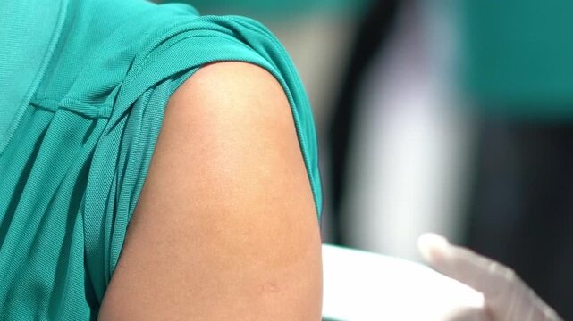 Nurse administering a vaccine injection into a patient's upper arm, followed by applying an adhesive bandage over the injection site.