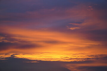 Fototapeta premium Breathtaking sunset sky with vibrant golden orange, yellow, and soft purple clouds. A peaceful natural background capturing twilight atmosphere, warm sunlight gradients, and tranquil evening beauty