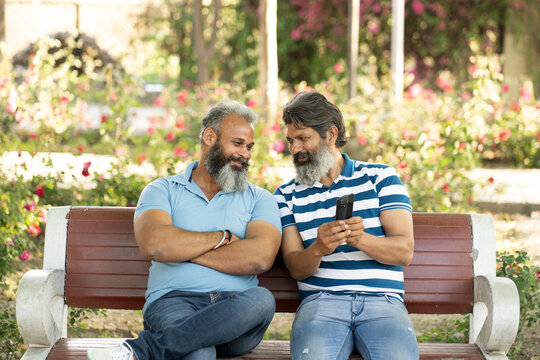 Two indian matured bearded male friends using mobile phone and spending leisure time at autumn park