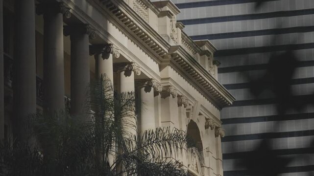 The sandstone colonnade of a heritage building in Brisbane stands beside the striped glass facade of a modern high rise tower.
