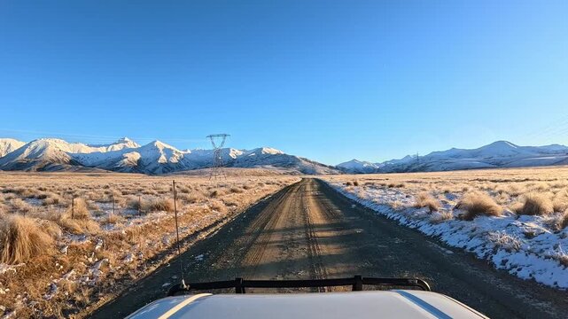 Front hood view of a 4x4 driving up gravel Rainbow Road toward sunlit snow-covered mountains on a clear winter day.