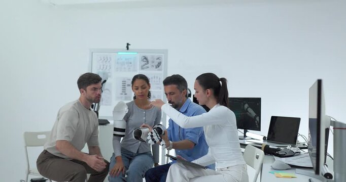 Engineering team in business casual examining robotic arm and hand in bright technology lab