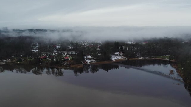 Lake Anten near Grafsnas with calm water and snow-covered wooded shoreline, Sweden, aerial dolly with low clouds hanging over trees