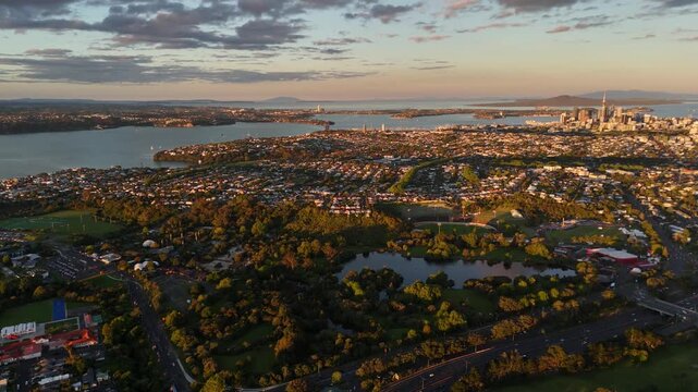 Bird&rsquo;s eye aerial establishing shot of Mount Albert Area and Auckland suburbs at sunset, featuring panoramic city views, residential neighborhoods, greenery and skyline.