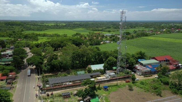 Sagay Negros midday cell tower drone shot panning right and orbiting the communication tower with solar panels behind a sugarcane plantation. The grid-tie solar setup generates power for the telecommu