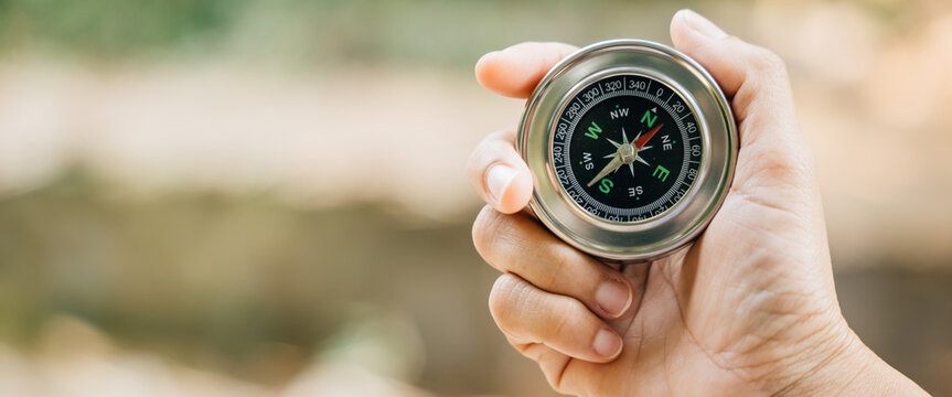 Traveler hand holds compass in park signifying her quest for guidance and direction. compass set against nature background represents exploration seeks to conquer defeat on her journey through forest.