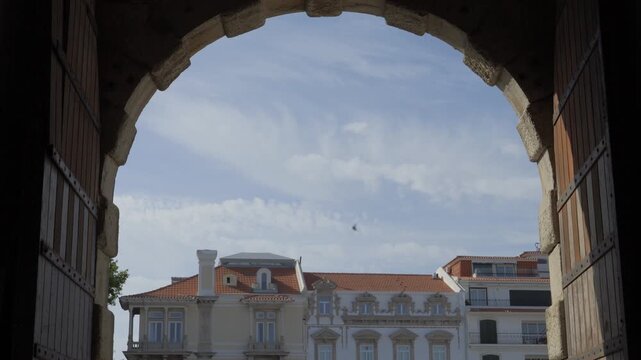 Stone gate arch of the Cascais Citadel framing historic facades and cloudy sky