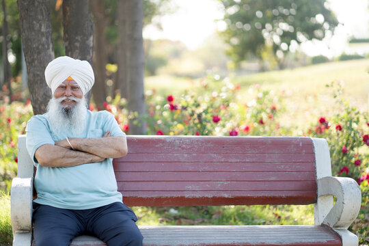 Indian sikh senior man feels happy while sitting on bench at park