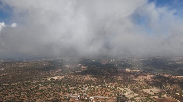 Cinematic drone footage flying through low clouds over the mountainous landscape of Anogyra.
