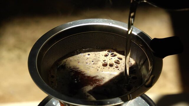Close-up video of hot water being poured gently over freshly ground coffee inside a stainless steel dripper filter.