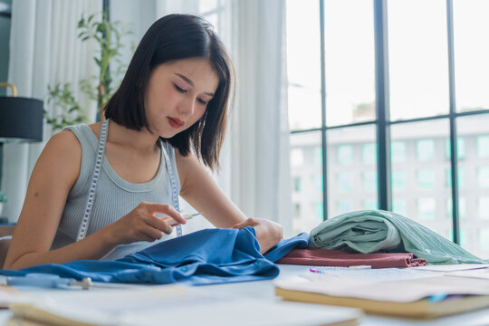 Asian woman tailor using scissors to cut off excess threads.