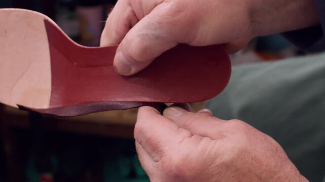Footwear craft. Diy manufacturing. Unrecognizable professional cobbler man hands working with leather material sole at workspace.