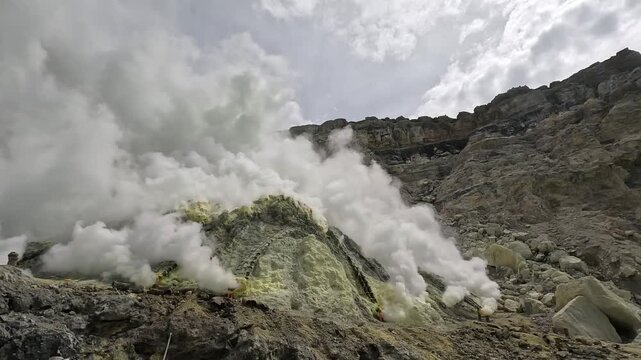 Active steaming fumaroles and yellow sulfur deposits on steep rocky cliffs at a volcanic mining site in Indonesia