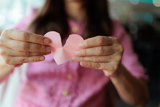 Sad Woman Hands Tearing Pink Paper Heart Close Up View. Unhappy female person rips a small sticky note symbol apart inside