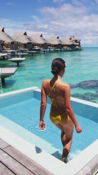 Luxury resort hotel woman walking on her private terrace deck of overwater bungalow with pool view on turquoise ocean - honeymoon suite. Raw vertical video of real woman model without makeup