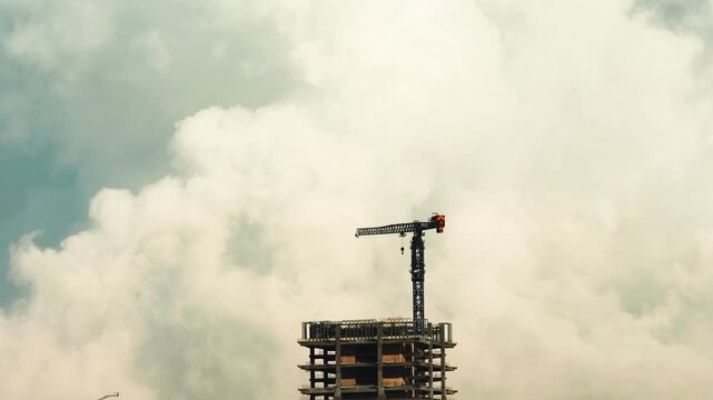 4k time lapse footage of crane on city buildings top with moving white clouds and blue sky background.